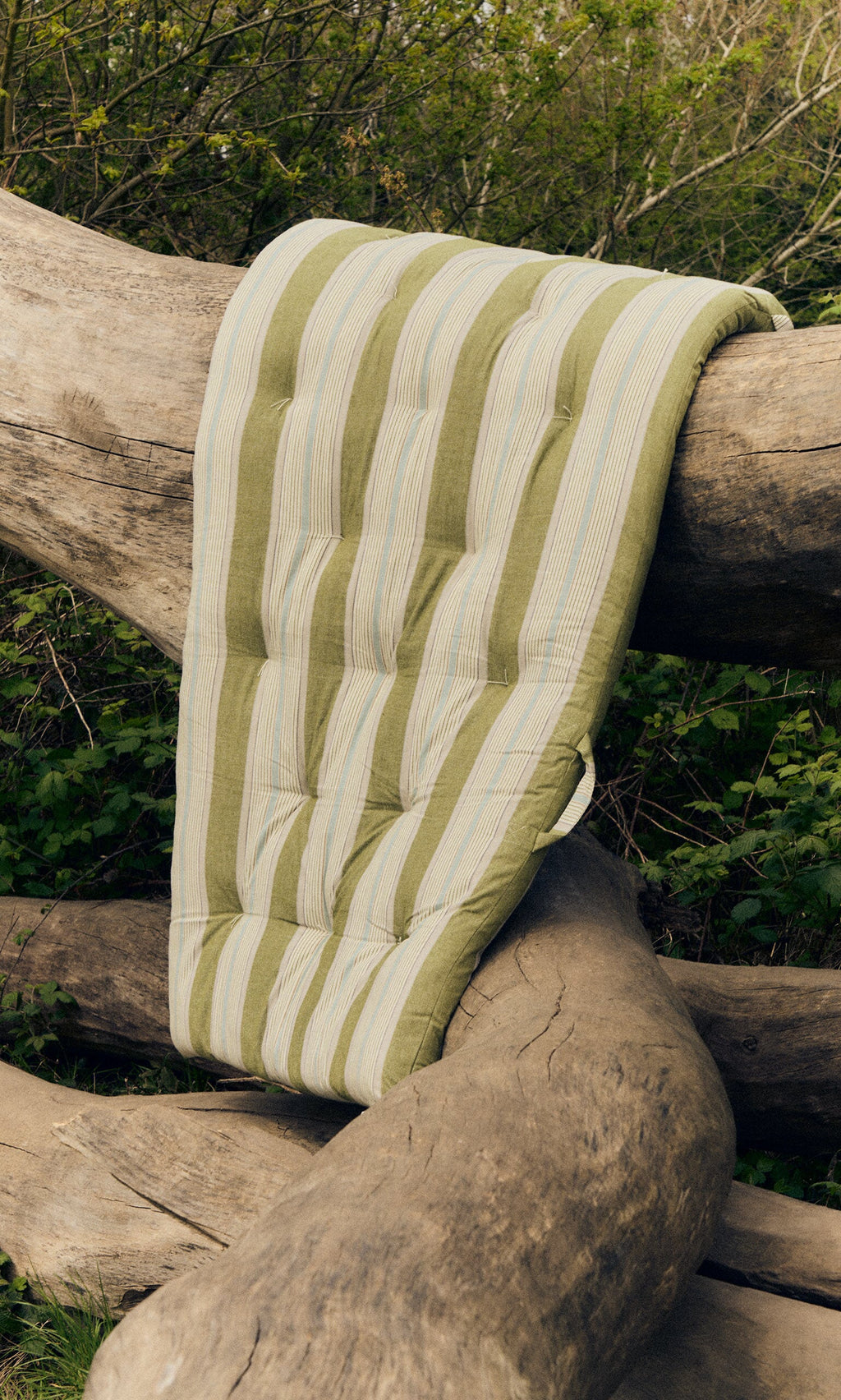 Plümo- The Quilted Mattress - Green Stripe is draped over large tree trunks outdoors for a sustainable look.