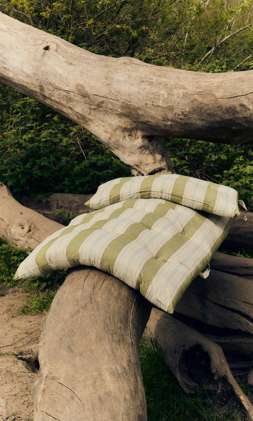 Plümo- Two Quilted Mattresses in Green Stripe are placed on intersecting tree trunks in a wooded area.