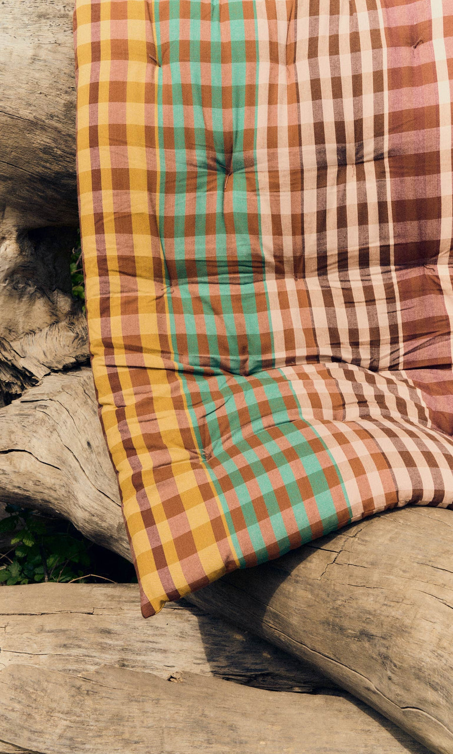Plümo- A red Quilted Mattress with a foldable design is draped over large, weathered logs.