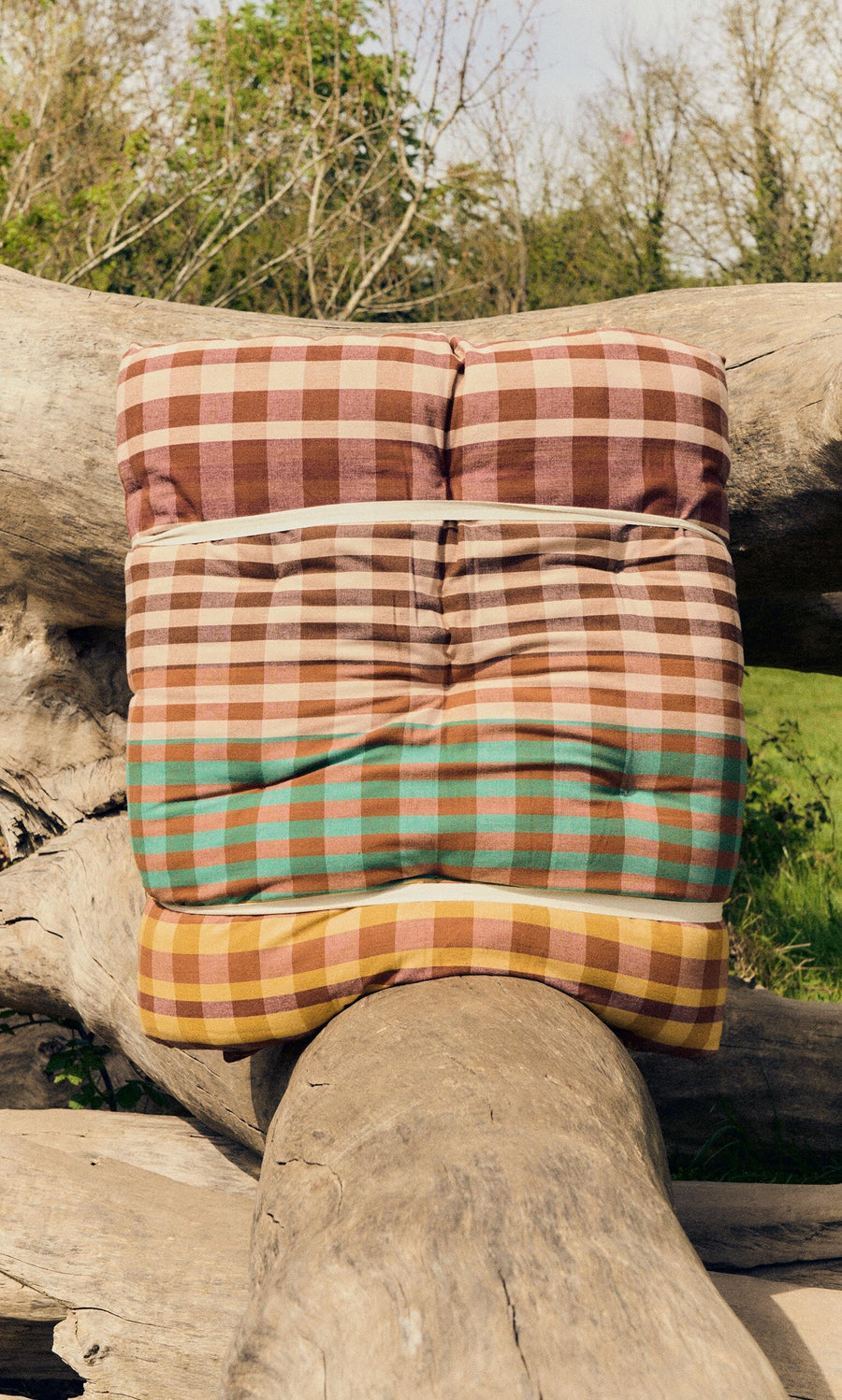 Plümo- A Quilted Mattress - Red rests on a large fallen tree trunk outdoors.