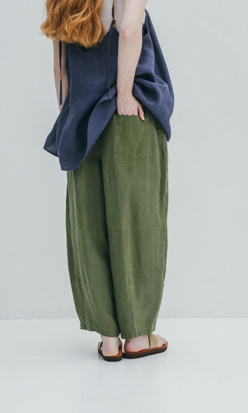 Plümo- Person with long red hair in a navy top and green Quincy Pants, standing against a light background.