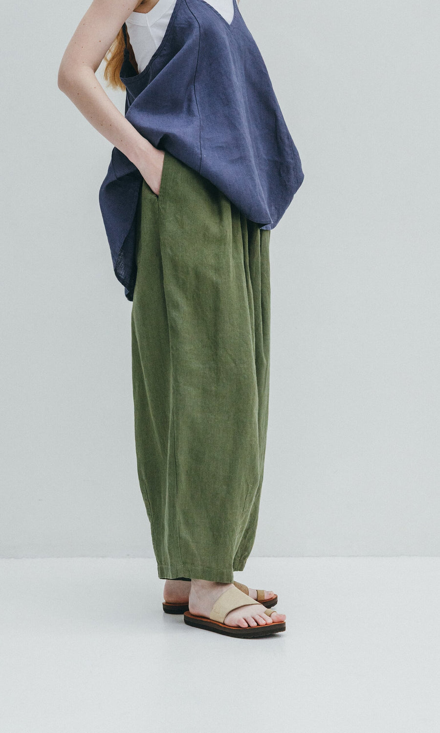 Plümo- Person wears loose green Quincy Pants with an elasticated waist, navy sleeveless top, and sandals.