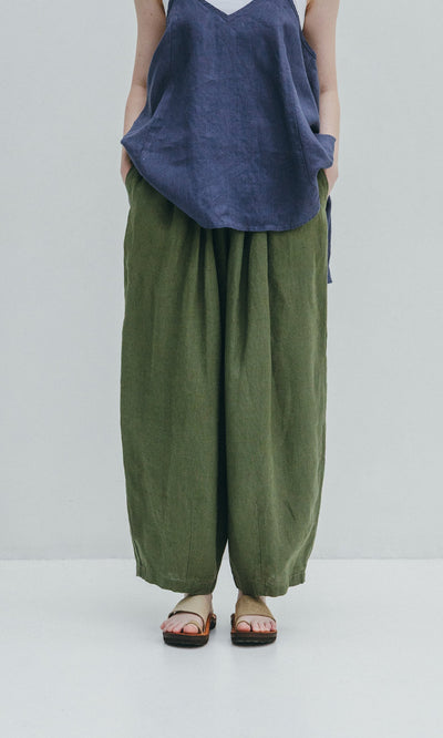 Plümo- Person in a blue sleeveless top, Quincy Pants in green linen with elasticated waist, and sandals against a light background.