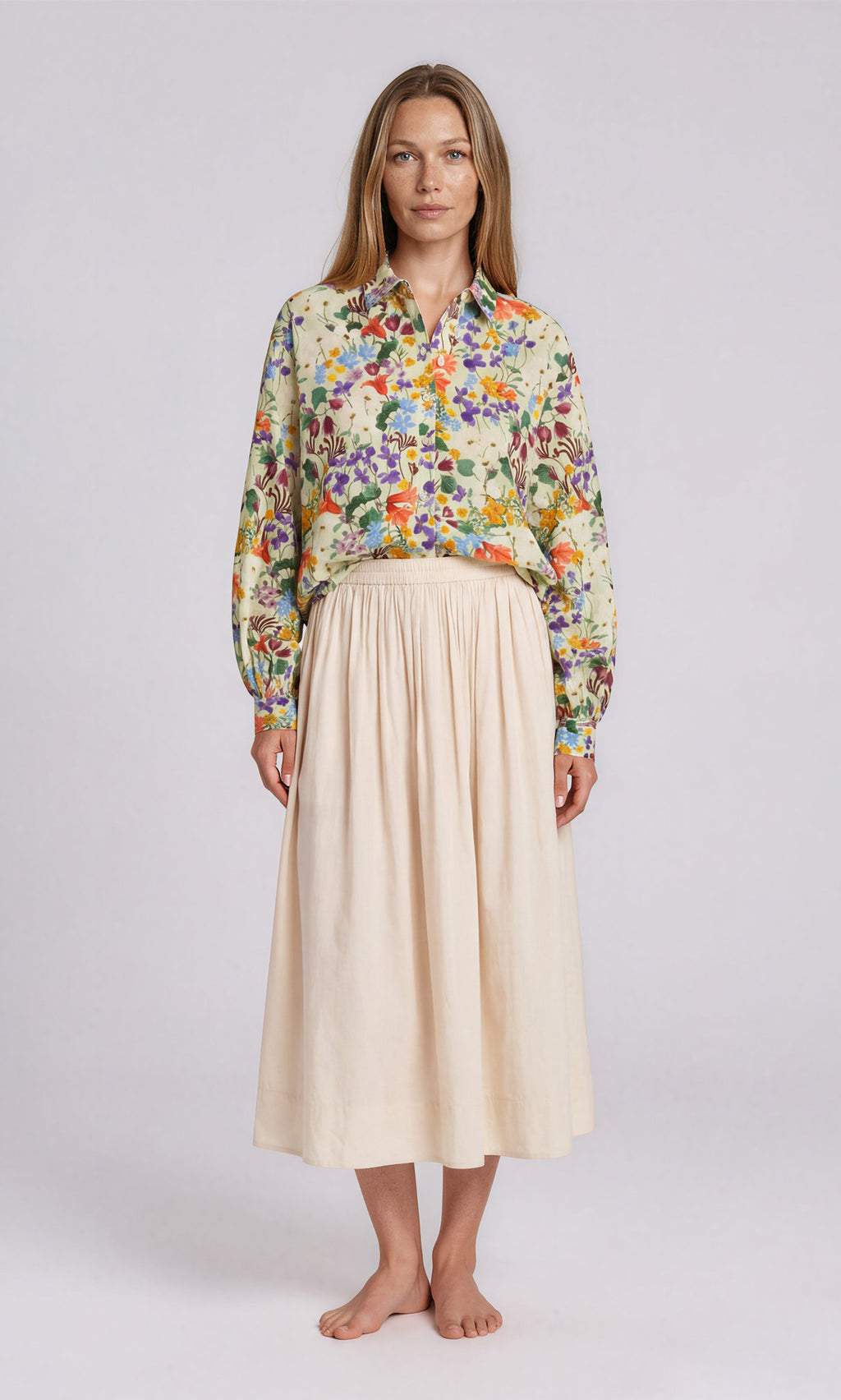Plümo  Woman in floral long-sleeve shirt and the light beige, high-waisted Rika Wide Skirt with slip pockets, barefoot.