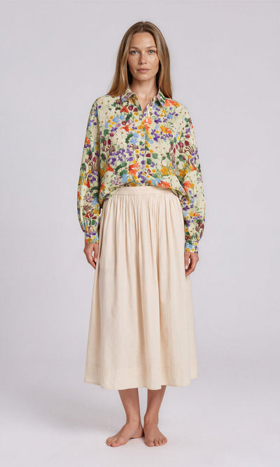 Plümo  Woman in floral long-sleeve shirt and the light beige, high-waisted Rika Wide Skirt with slip pockets, barefoot.