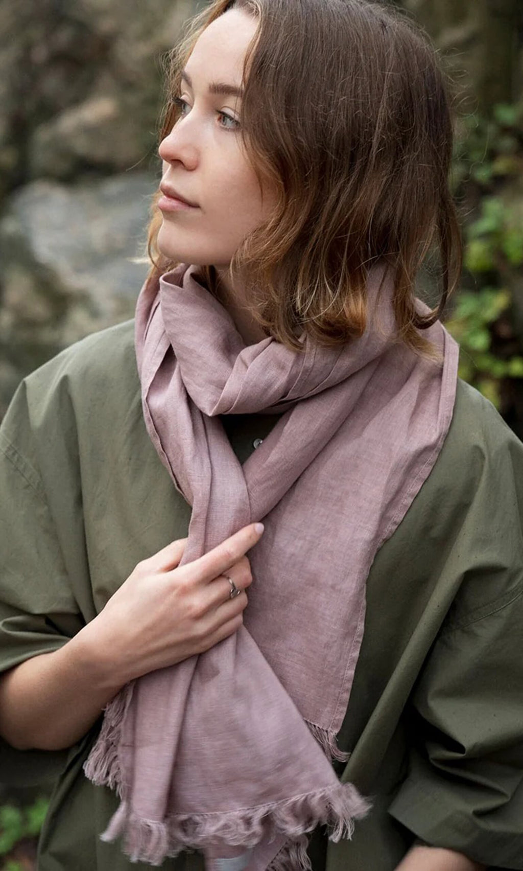 Plümo- Woman outdoors touches her Rosie Scarf, styled with selvedge fringe, paired with a green top.