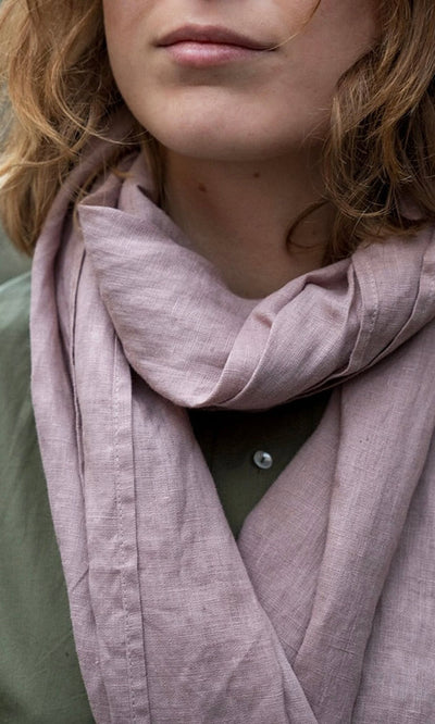Plümo- A person with wavy hair wears the Rosie Scarf in faded rose and an olive green shirt, shown from the shoulders up.