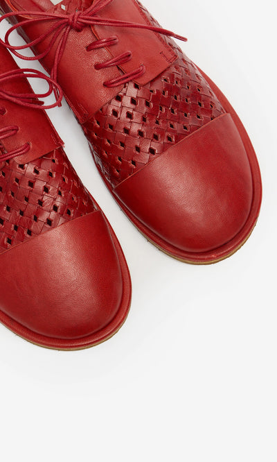 Plümo- Close-up of Magui Brogues—red Italian leather shoes with woven details and laces, set against a white background.
