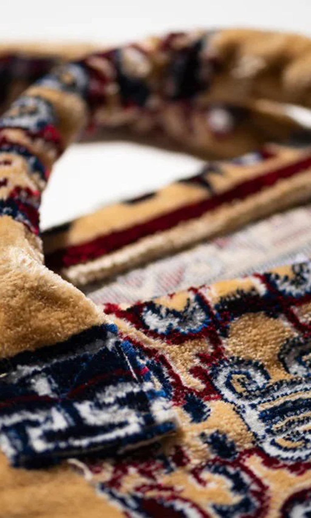 Plümo- Close-up of the Rug Bag - Antik Gold, featuring patterned blue, red, and beige designs with folded textured edges.