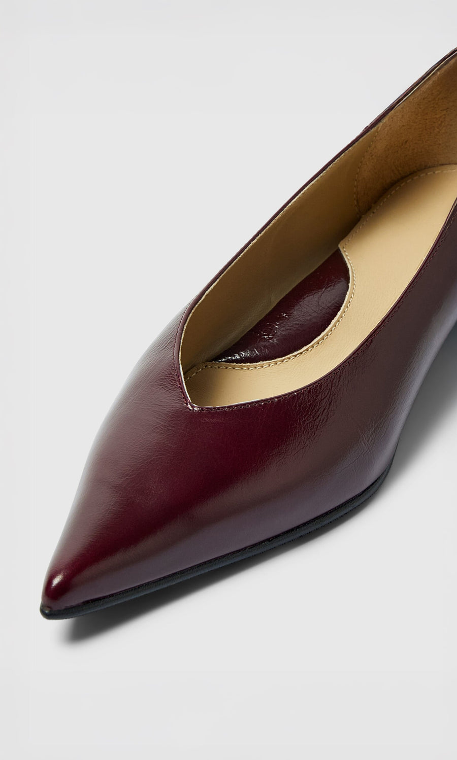 Plümo- Close-up of Jan Pumps, a burgundy pointed-toe leather flat with low block heel, against a light background.