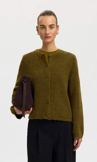 Plümo  A woman in a Lucinda Cardigan, moss green, holds a brown bag against a plain white background.