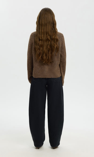 Plümo  Person with long wavy brown hair wearing the Findlay Cardigan and loose black pants, standing facing away.