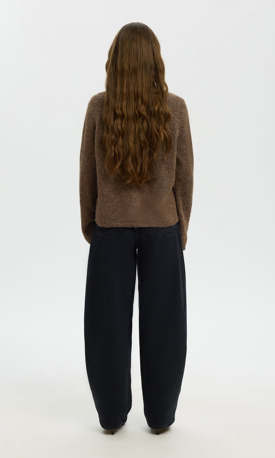 Plümo  Person with long wavy brown hair wearing the Findlay Cardigan and loose black pants, standing facing away.