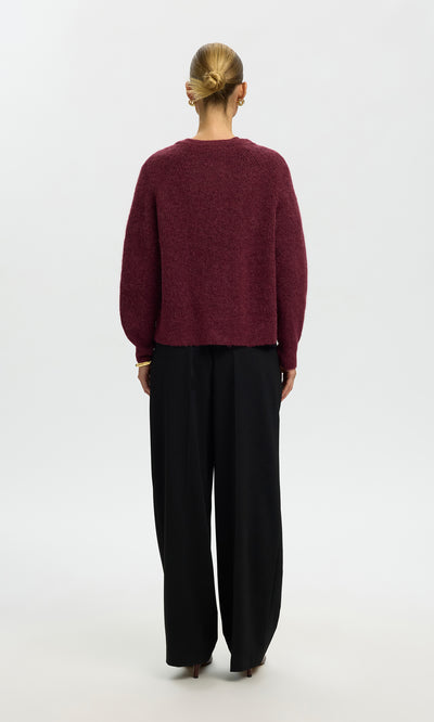 Plümo  Model faces away in the Caen Cardigan - Jam and loose black pants against a plain white background.