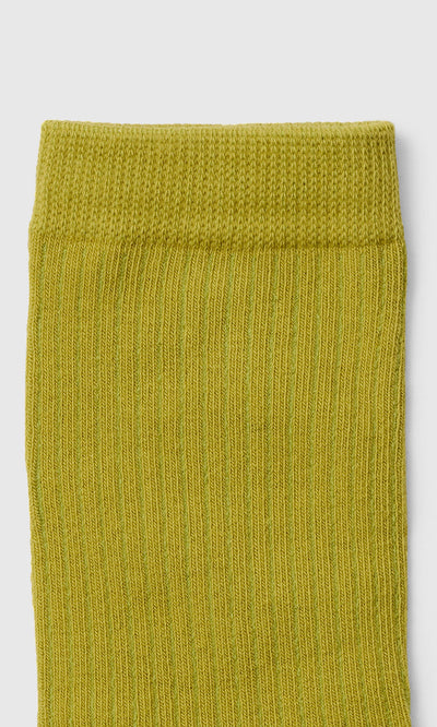 Plümo  Close-up of the top part of a rib-knit, bright green sock against a white background.