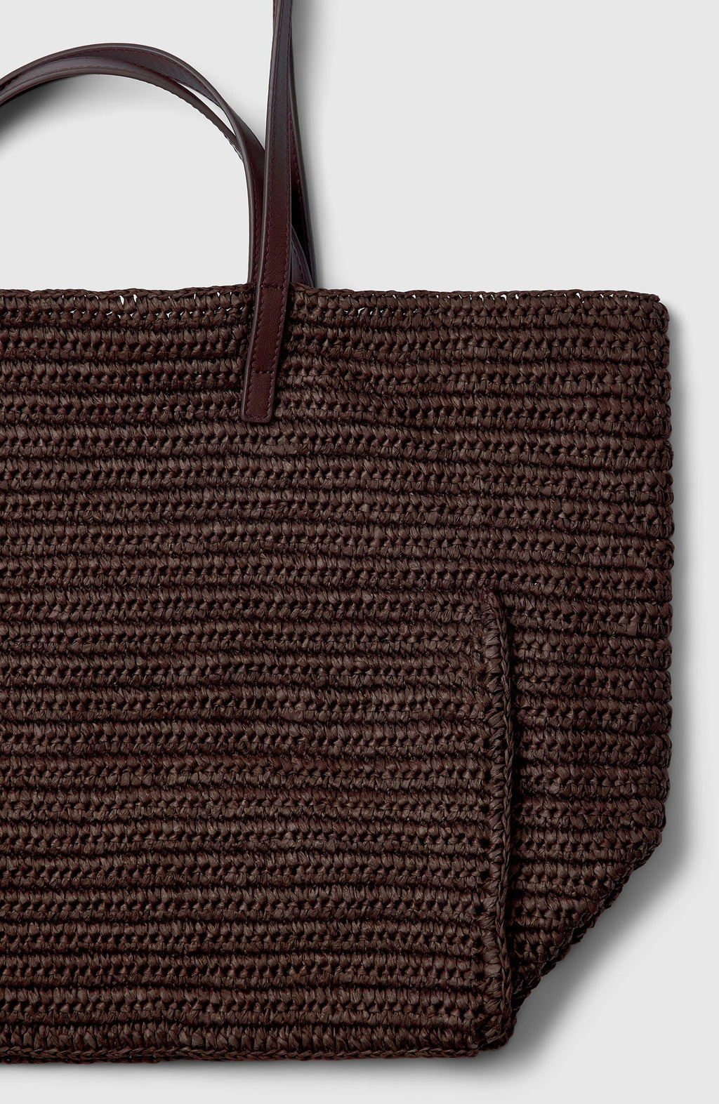 Plümo- Close-up of the Tova Bag, a brown straw tote with dark leather handles and a boxy design on a light gray background.