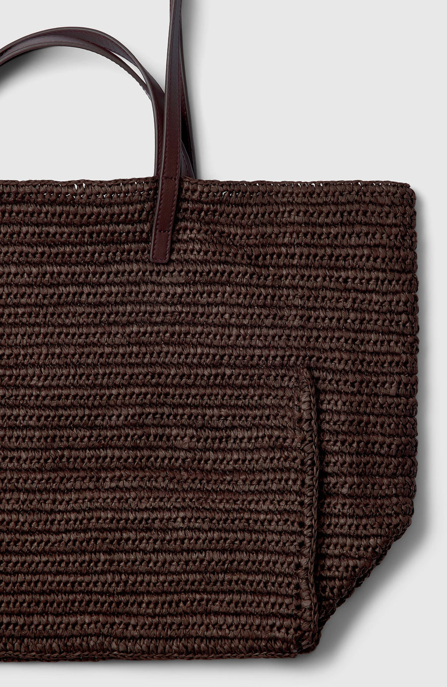 Plümo- Close-up of the Tova Bag, a brown straw tote with dark leather handles and a boxy design on a light gray background.