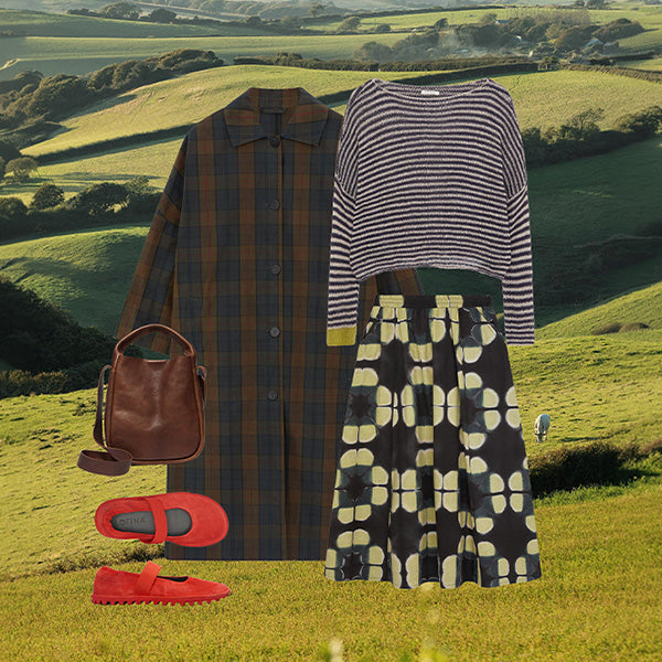 Plümo- Collaged outfit with plaid coat, striped sweater, printed skirt, brown bag, and red shoes over a green countryside background.