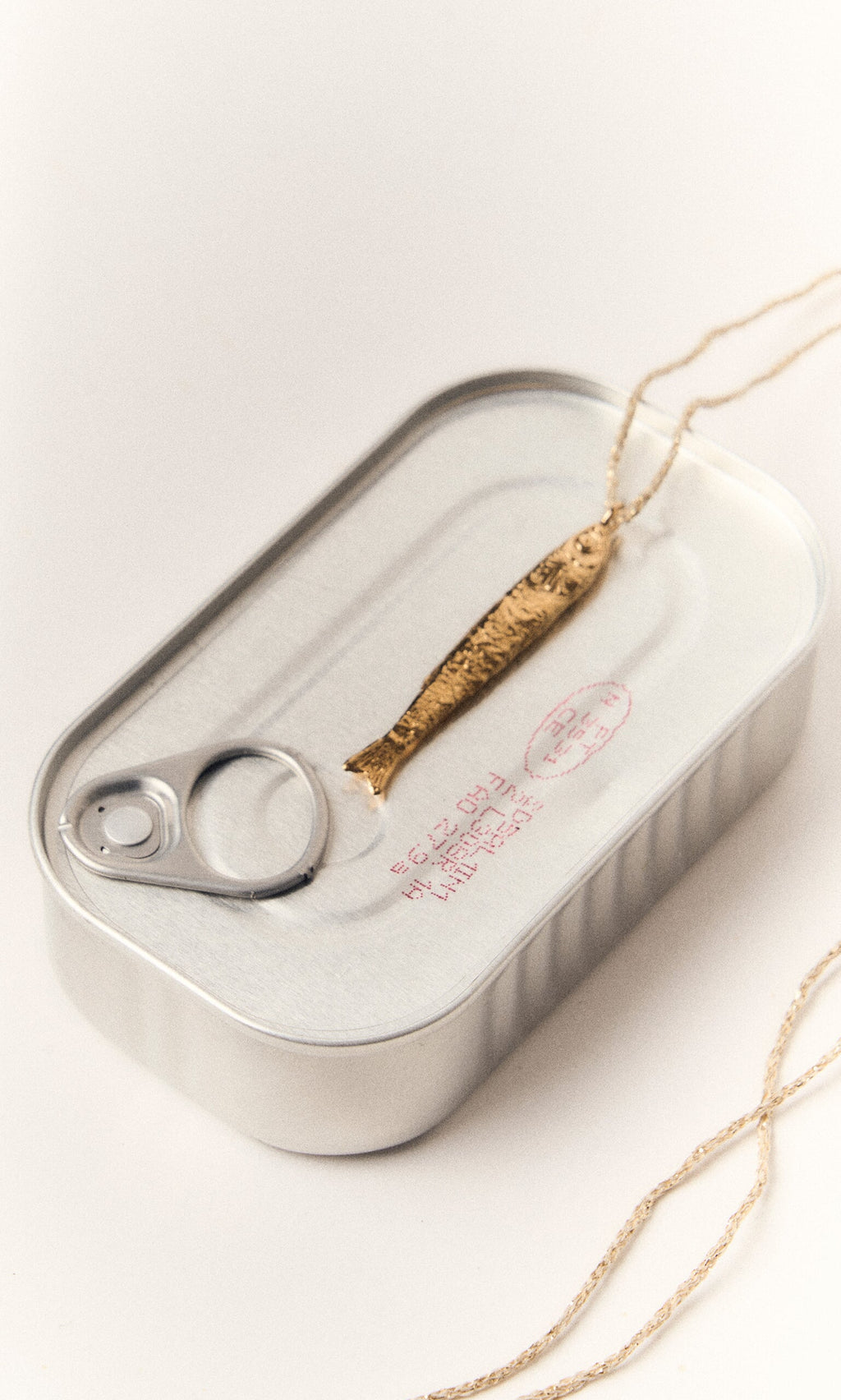 Plümo- The Sardine Necklace features a gold-plated sardine pendant on a chain atop a closed silver tin can.