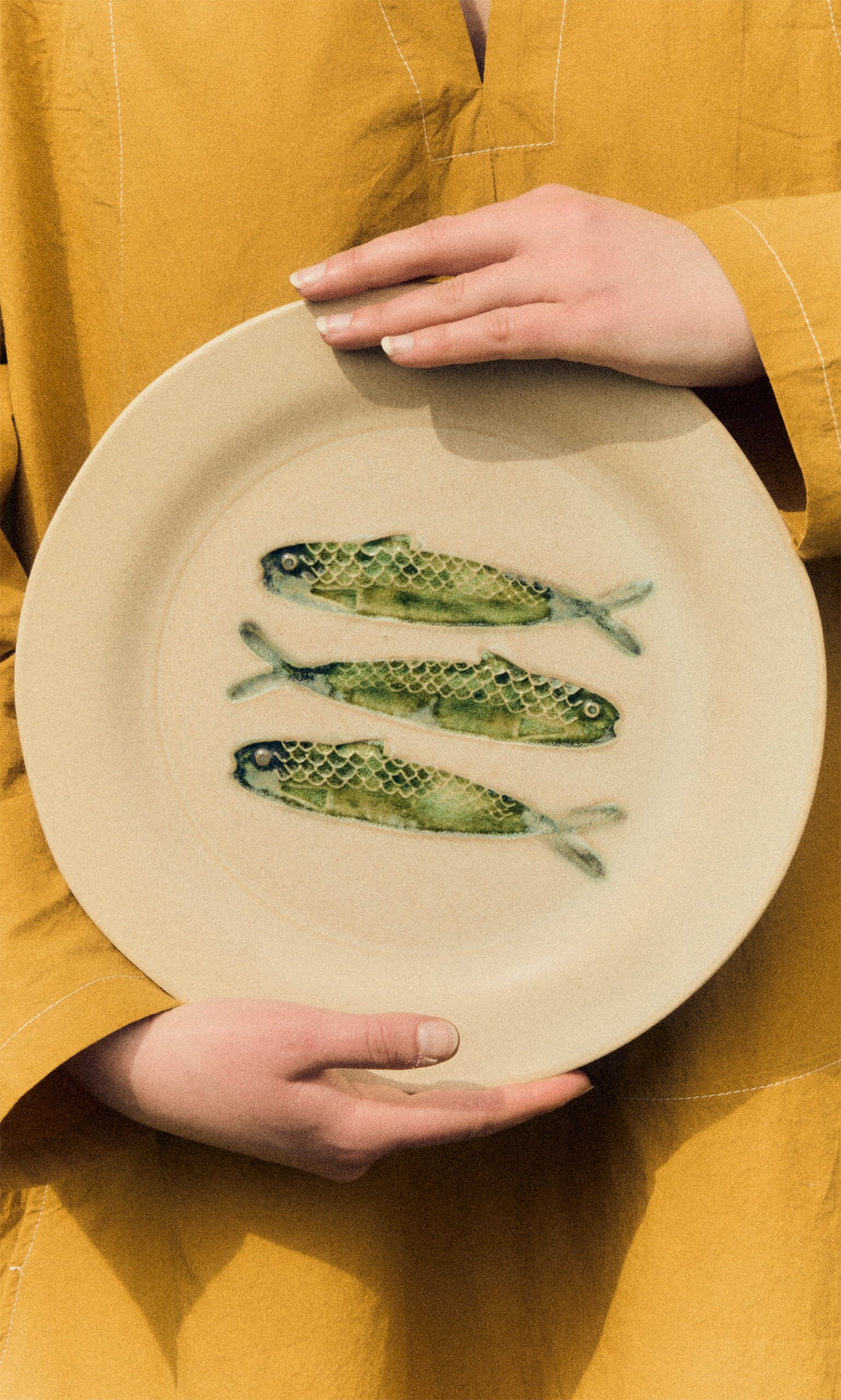 Plümo- Person in a yellow outfit holding the Sardine Plate, featuring three hand-painted sardines in the center.