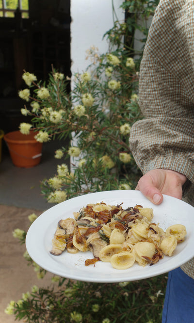 Plümo  Holding Vegetable Recipes By Jess Dennison, someone enjoys pasta surrounded by flowers and fresh greenery.