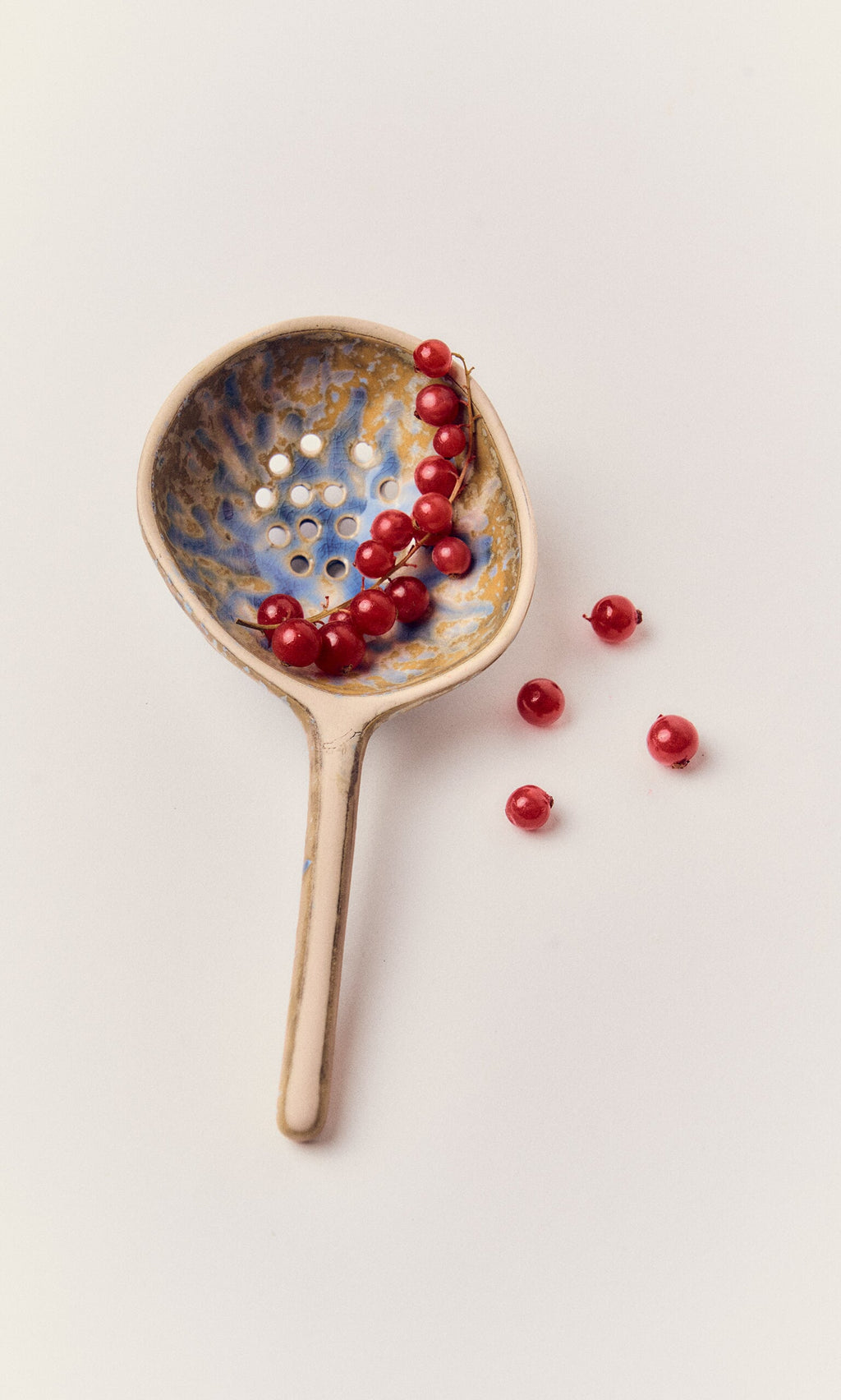 Plümo- A handmade Serving Spoon holds red currants, with a few beside it on a white background.