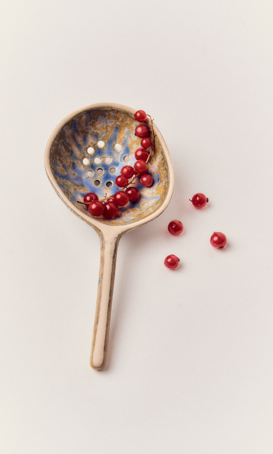Plümo- A handmade Serving Spoon holds red currants, with a few beside it on a white background.