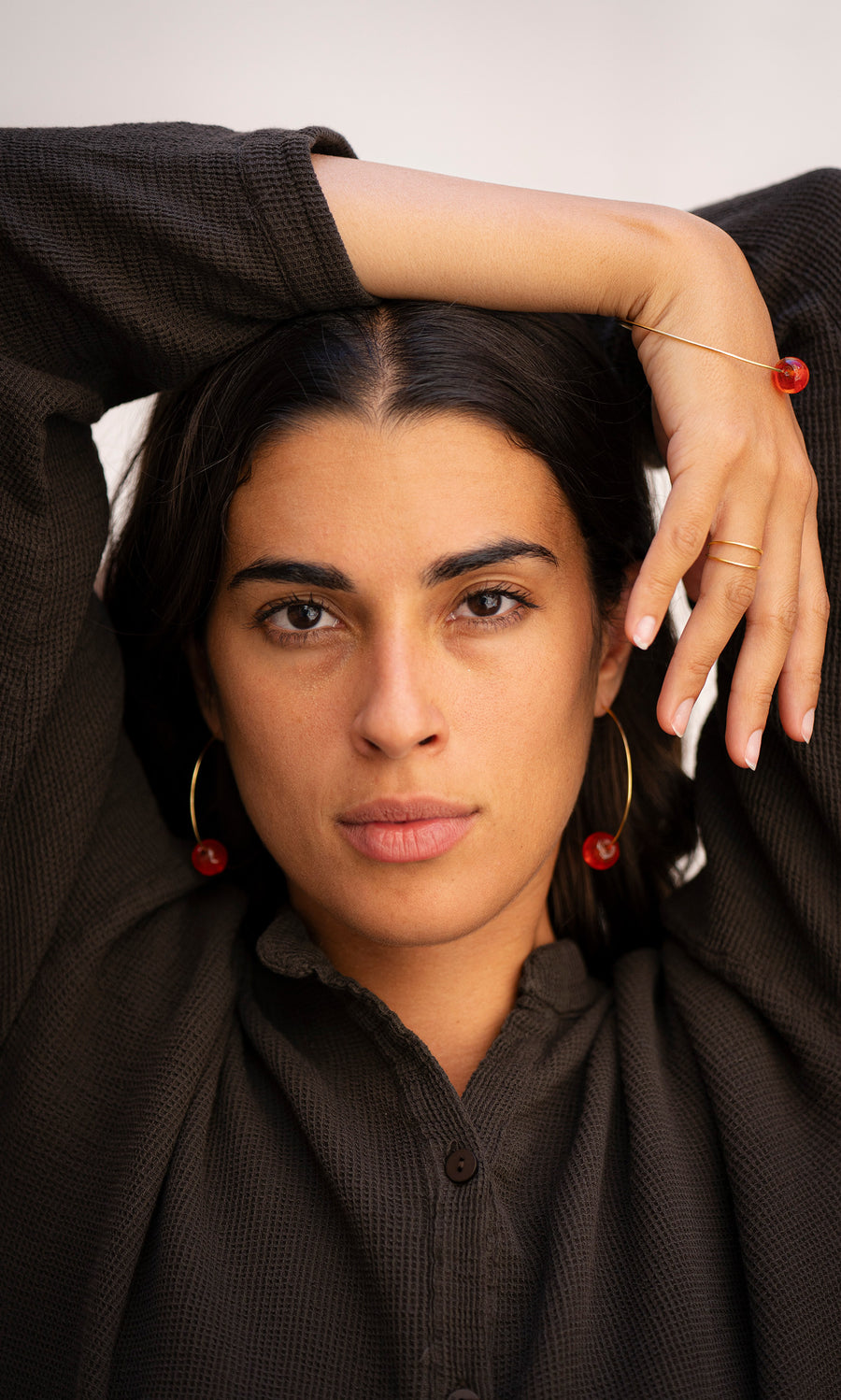 Plümo  Woman with dark hair models Clementine Earrings, one arm raised, wearing a brown textured top.