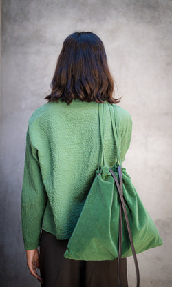 Plümo  A person in a green top carries a Velour Triangle Bag with a drawstring closure, facing away.