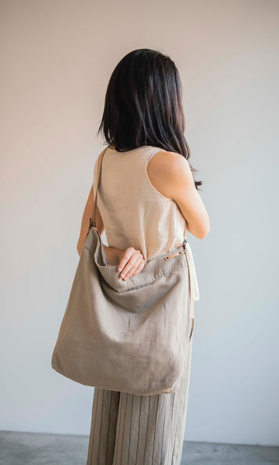 Plümo  Woman with long dark hair stands with her back turned, carrying the Paloma Bag, a large cotton-canvas tote.