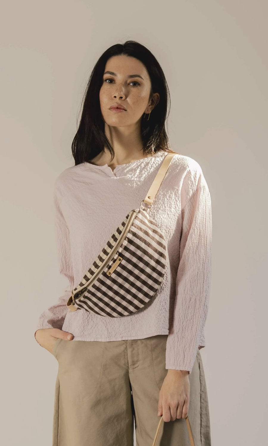 Plümo- Woman wearing a light pink blouse, tan pants, and the Gingham Bag with an adjustable leather strap.