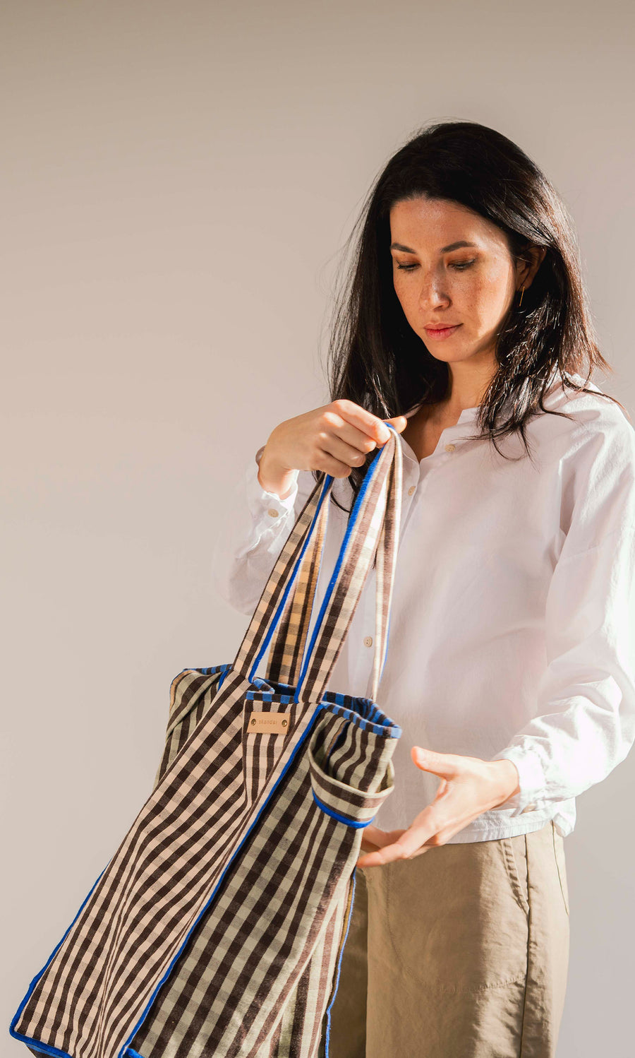 Plümo  Woman in a white shirt looks into the spacious Stylist Bag tote against a plain background.