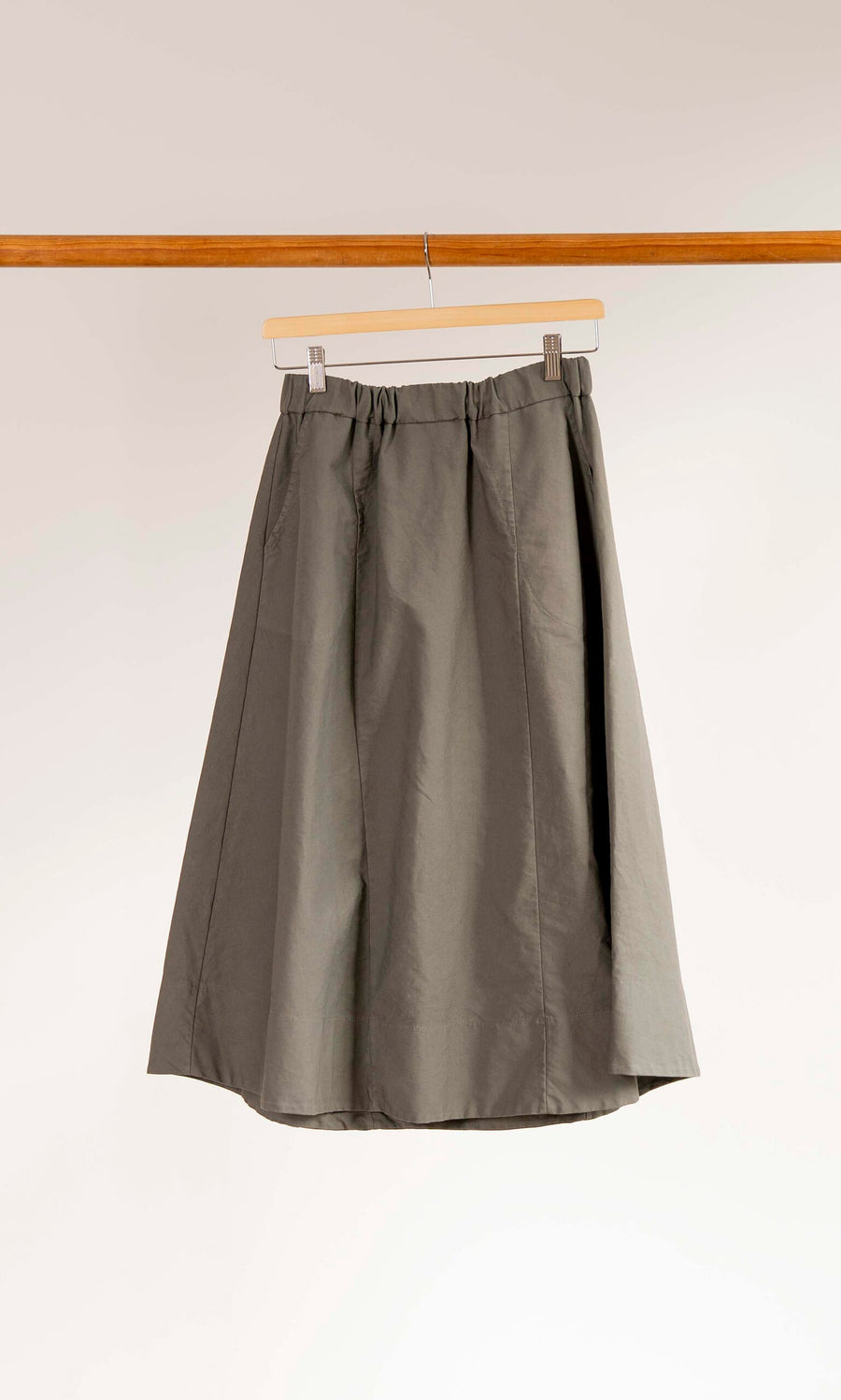 Plümo- The Marian Skirt, a gray cotton A-line with an elastic waist, hangs on a wooden hanger against a white background.