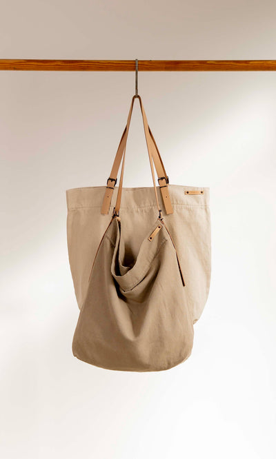 Plümo  Two Paloma Bags with tan leather straps hang from a rod. Beige cotton-canvas. Made in Barcelona.