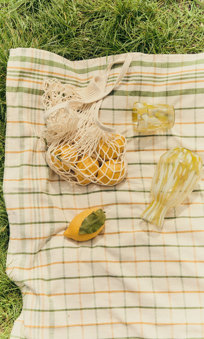 Plümo- Speckled Glass Jug - Yellow, handmade glasses, and lemons in a net bag on a plaid blanket on grass.