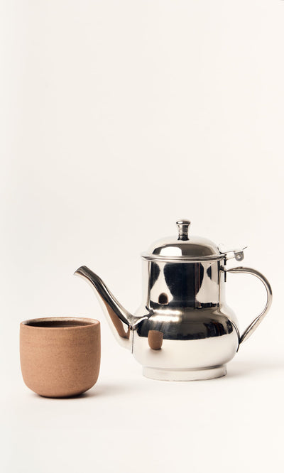 Plümo- A Steel Teapot with an industrial finish sits beside a plain brown ceramic cup on a white background.