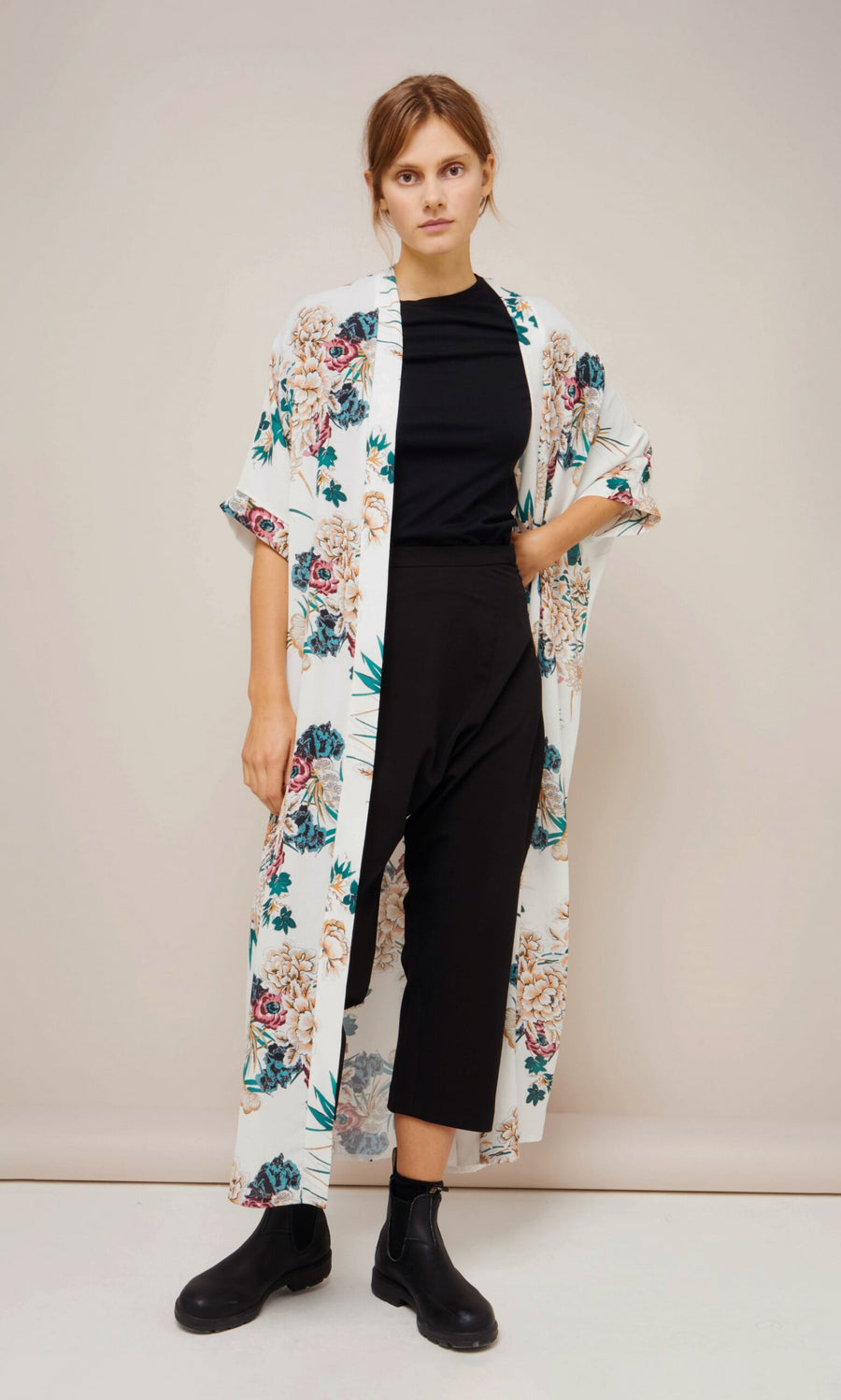 Plümo- Woman in black outfit with Tenny Kimono and black ankle boots, standing against a plain background.