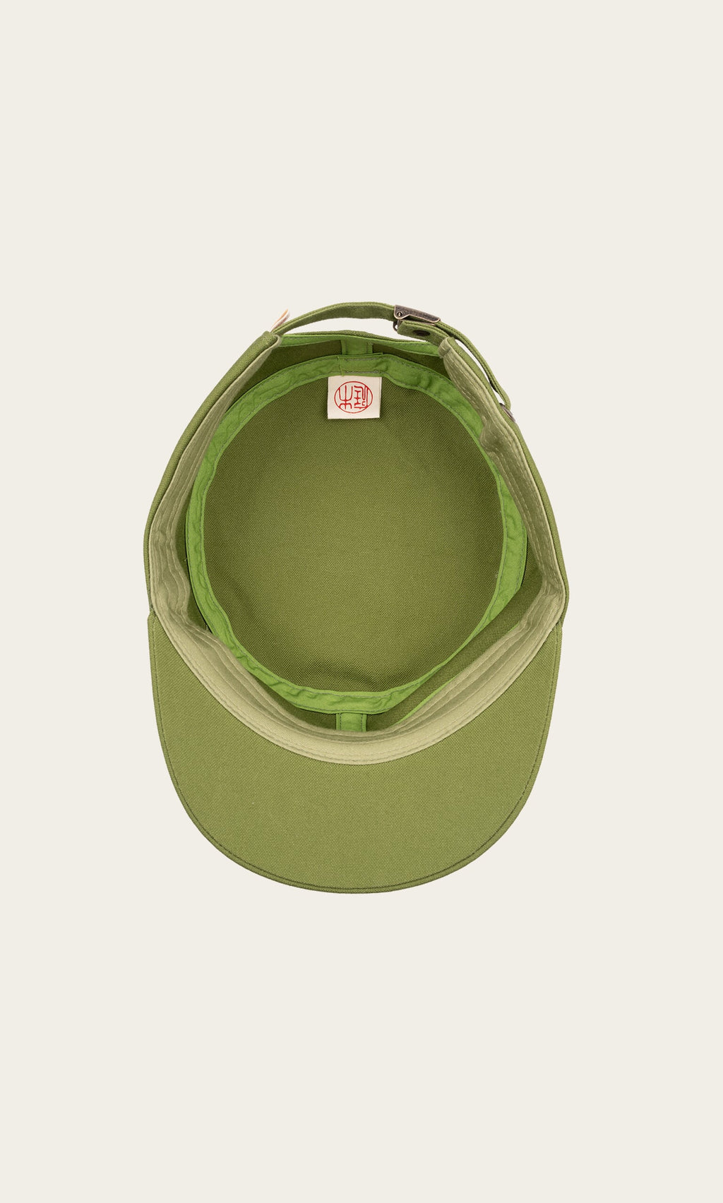 Plümo- Top view of the green Tsuba Cap, Hanpu canvas with curved brim and interior tag, handmade in Kyoto on off-white background.
