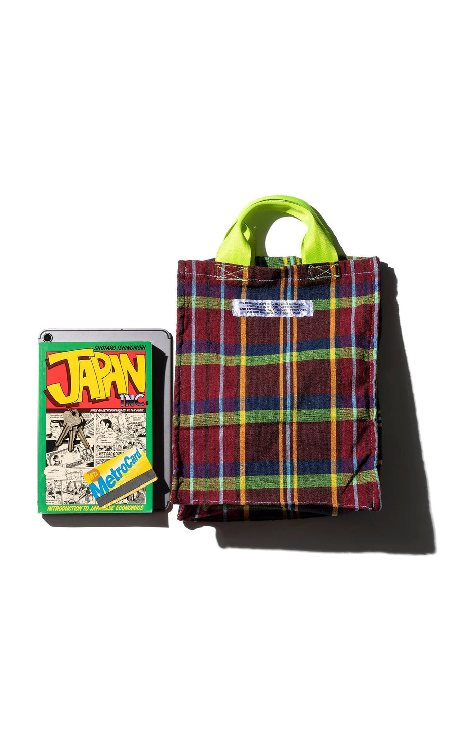Plümo- A Tartan Document Holder with green handles sits next to a comic book and MetroCard.