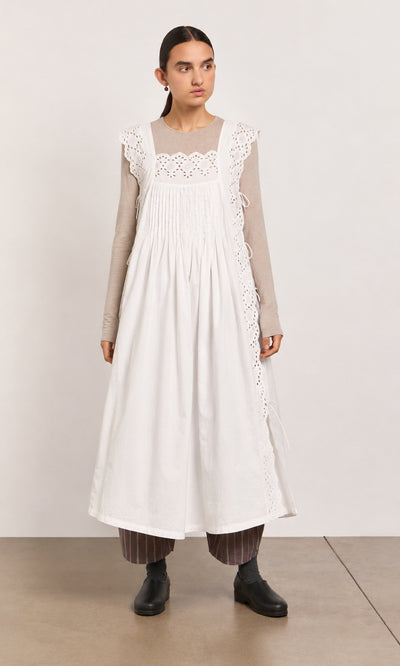 Plümo  Woman wears a Vintage Lace Dress - White over a beige top, striped pants, and black shoes, standing indoors.