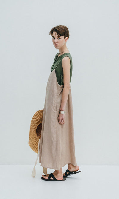 Plümo- Person in the Violet Dress, a sleeveless beige linen slip dress with a green top and adjustable fit, holding a wide-brimmed hat.