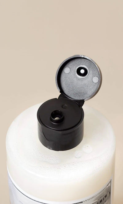 Plümo- A close-up of a Wool & Silk Detergent bottle with a black flip-top cap, partially open, foam on its white surface.