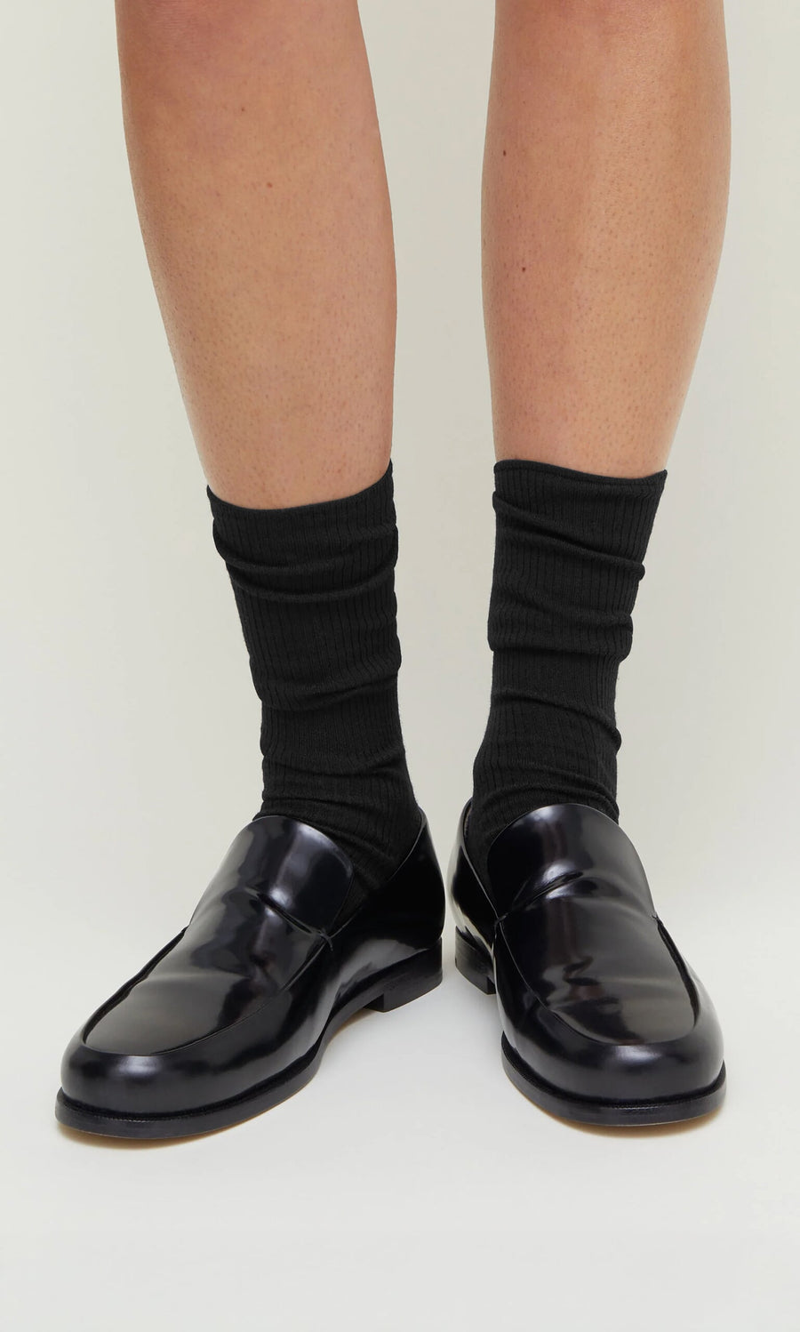 Plümo- Person wearing Black Rib Socks and black loafers, standing on a light-colored surface.