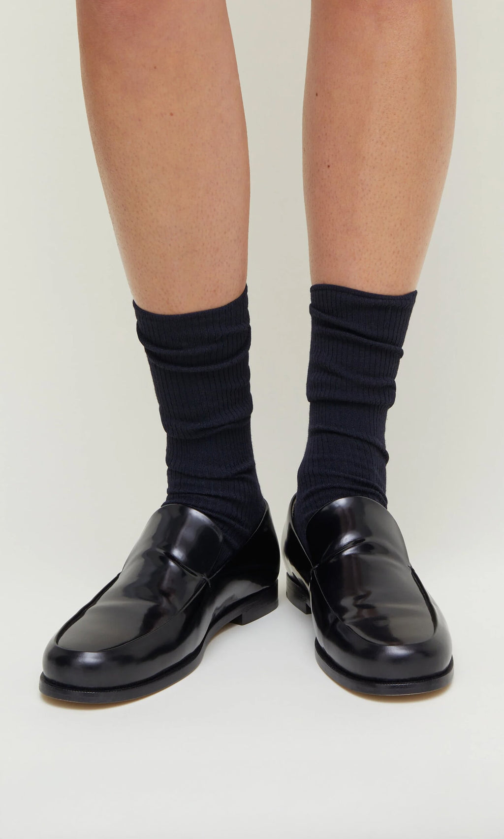 Plümo- Navy rib socks worn with shiny black loafers on a person's feet, standing on a light background.