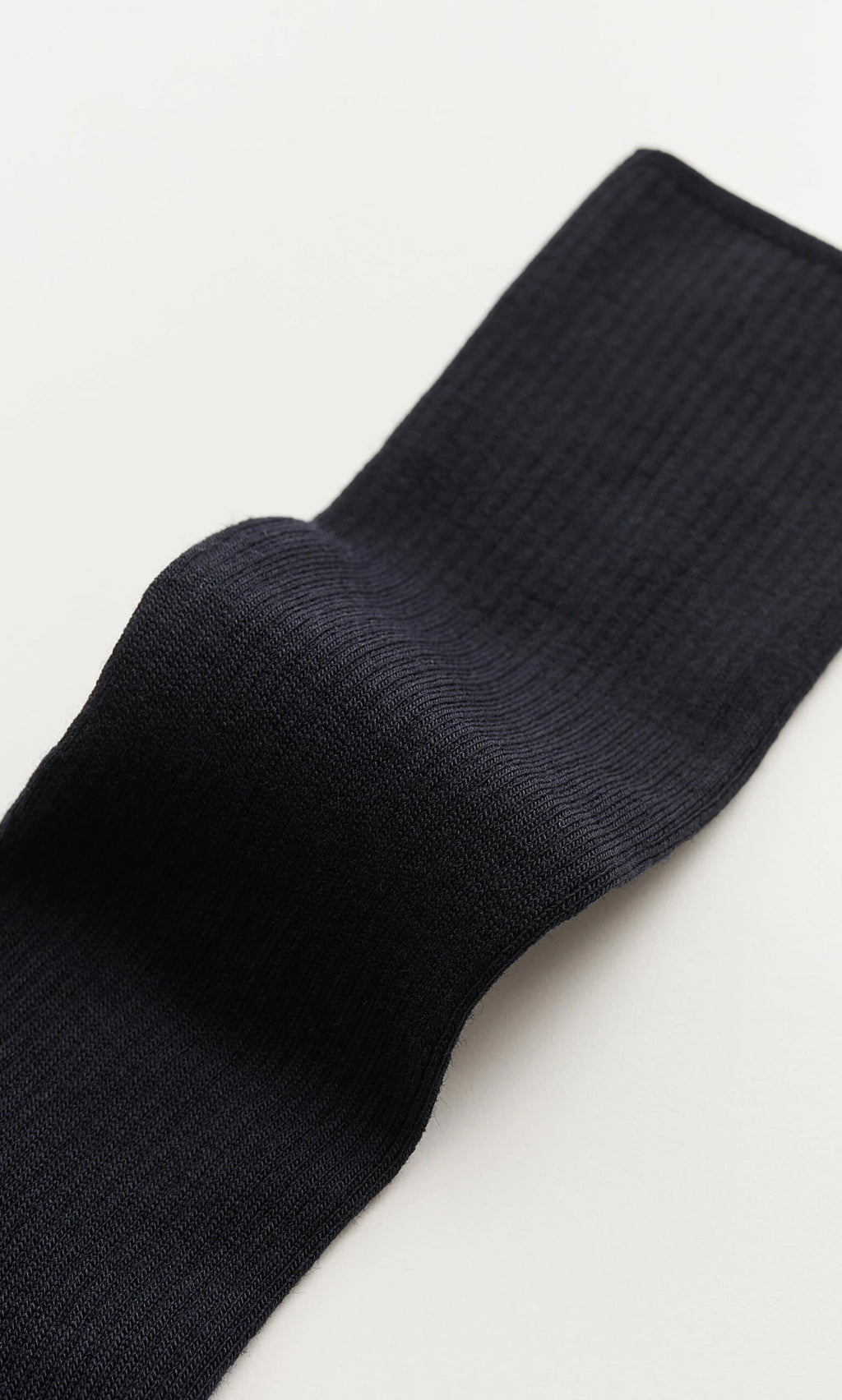 Plümo- A close-up of a navy rib-knit sock lying on a light surface.