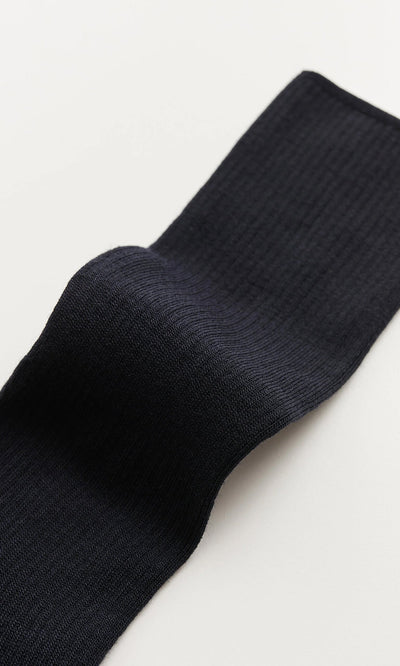 Plümo- A close-up of a navy rib-knit sock lying on a light surface.