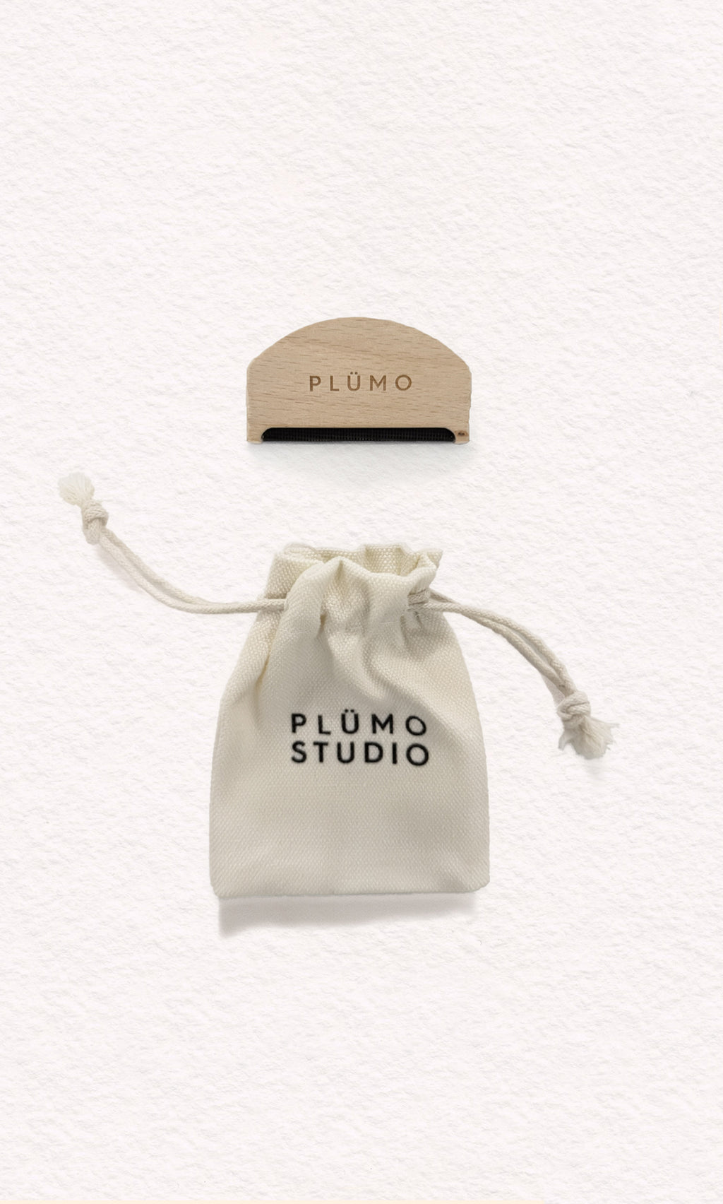 Plümo  A Wool Comb rests above a PLÜMO STUDIO pouch on a white textured background.