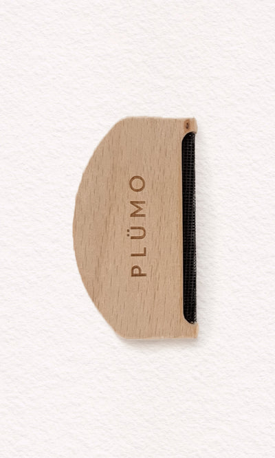Plümo  The Wool Comb, with PLÜMO engraving and metal edge, removes pilling; shown on white background.