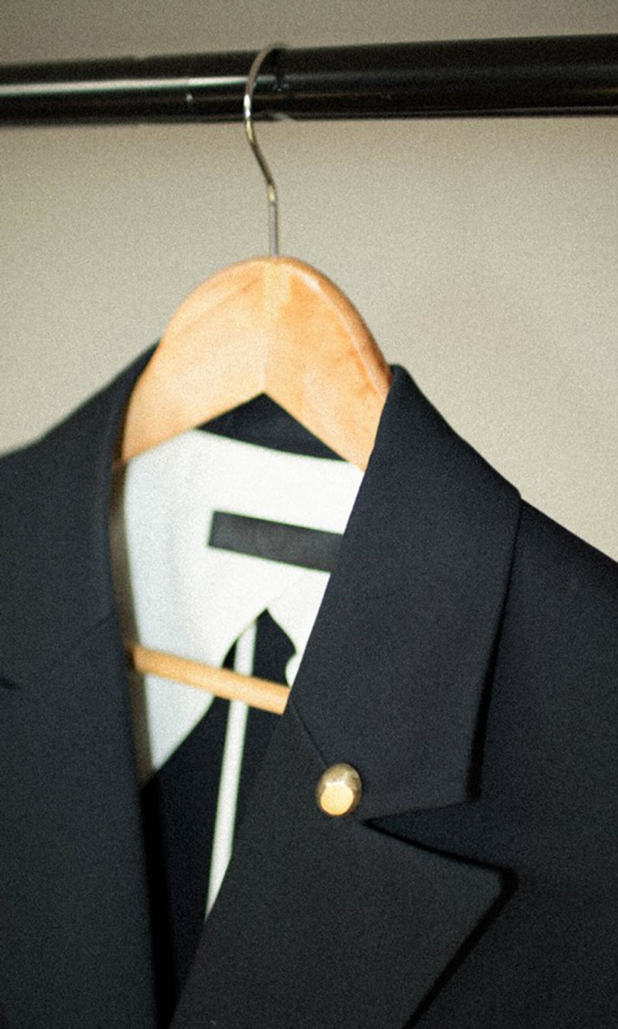 Plümo- A black suit and tie with the Amara Brooch on a wooden hanger, displayed on a metal clothing rack.