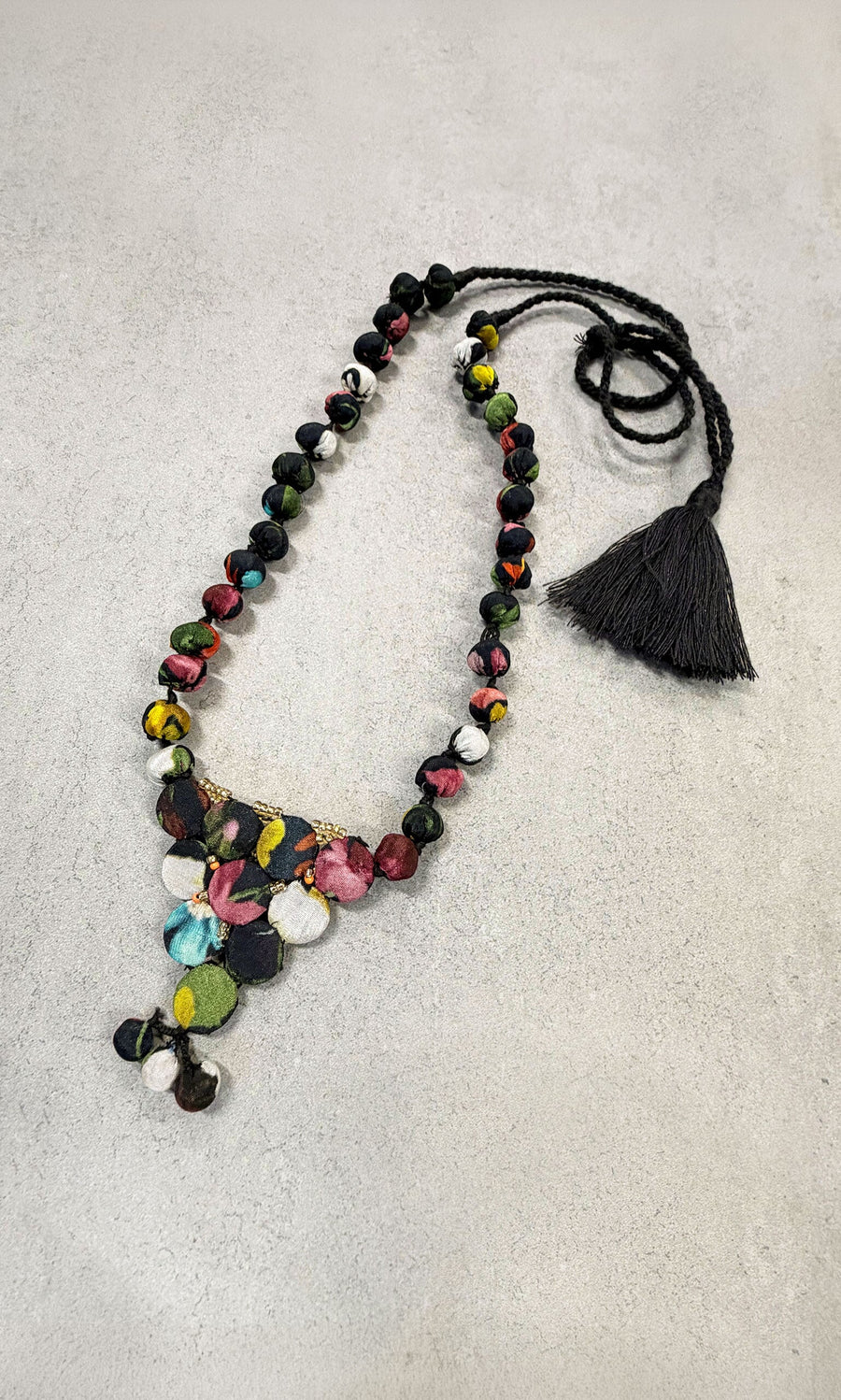 Plümo- Celia Choker Necklace with colorful beads, floral patterns, and black tassel displayed on a light gray surface.